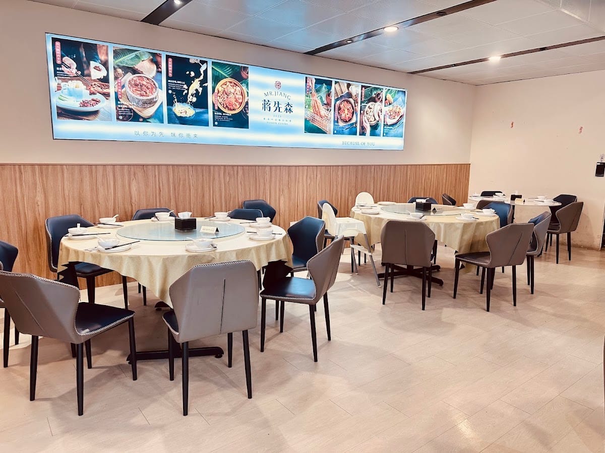 Mr Jiang's dining room: round tables with cream cloths and grey leather chairs under a lit 蒋先森 banner