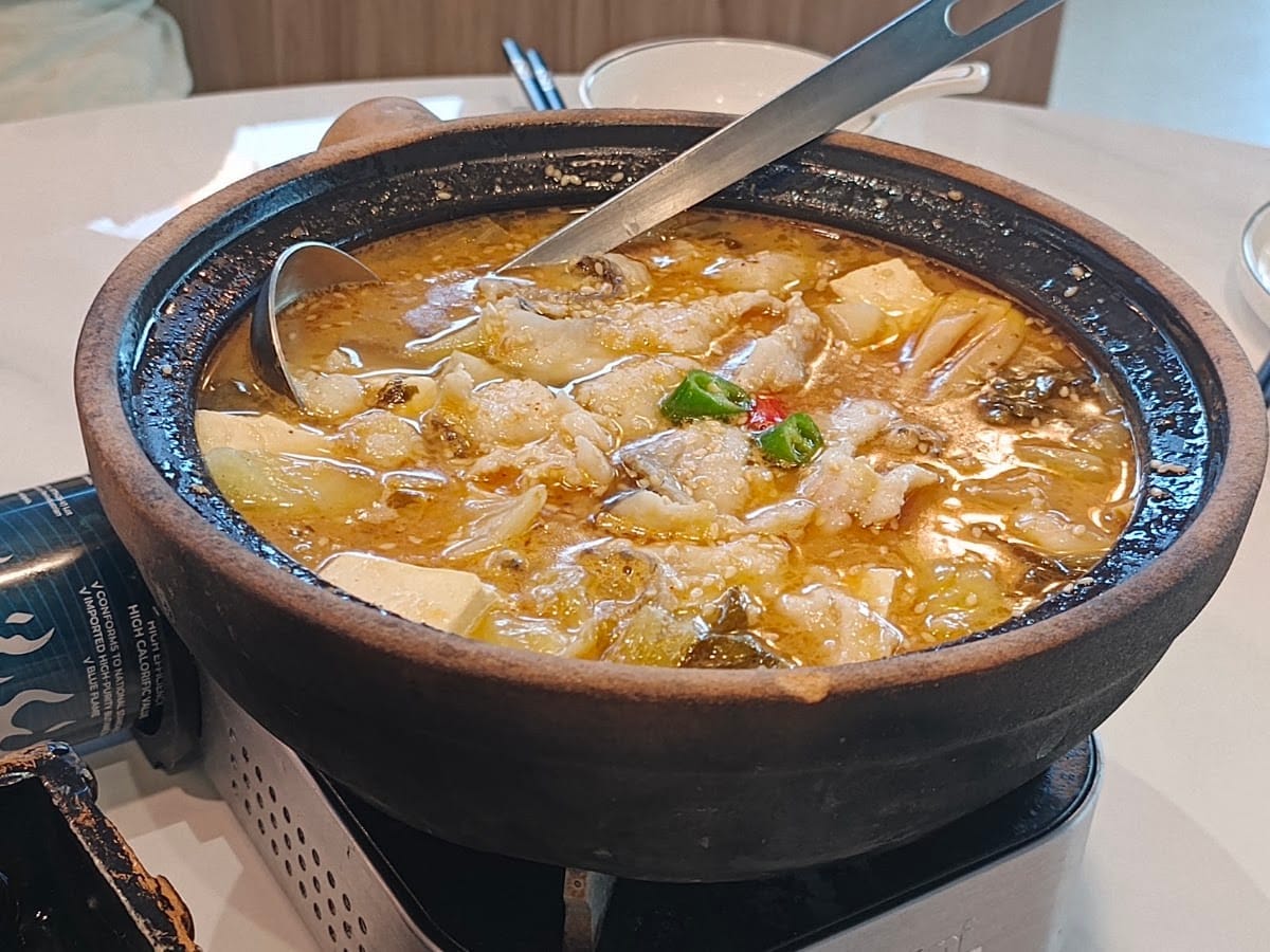 Sliced fish and tofu in a golden broth with chilli, in a clay pot on a tabletop burner