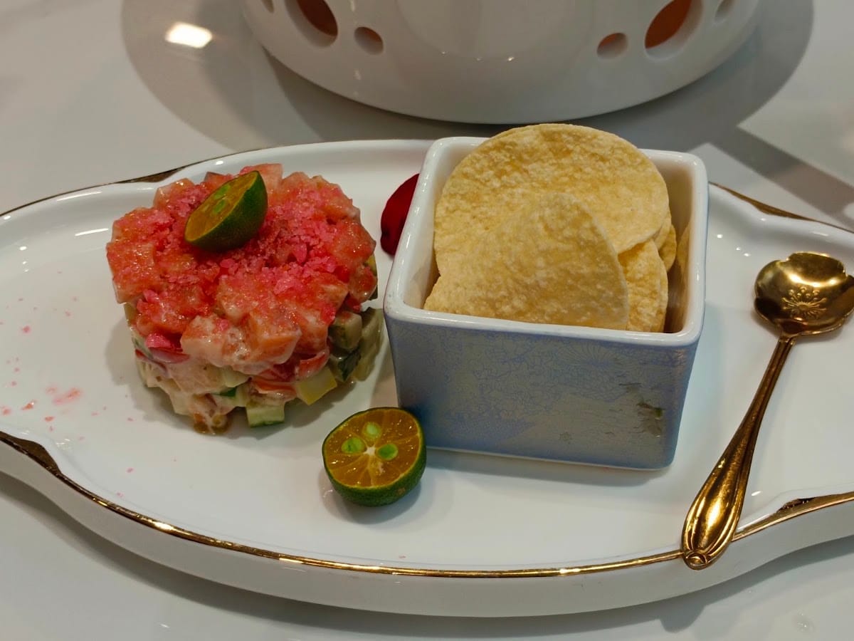 Diced salmon with cucumber and calamansi, served with crisps on a gold-rimmed plate